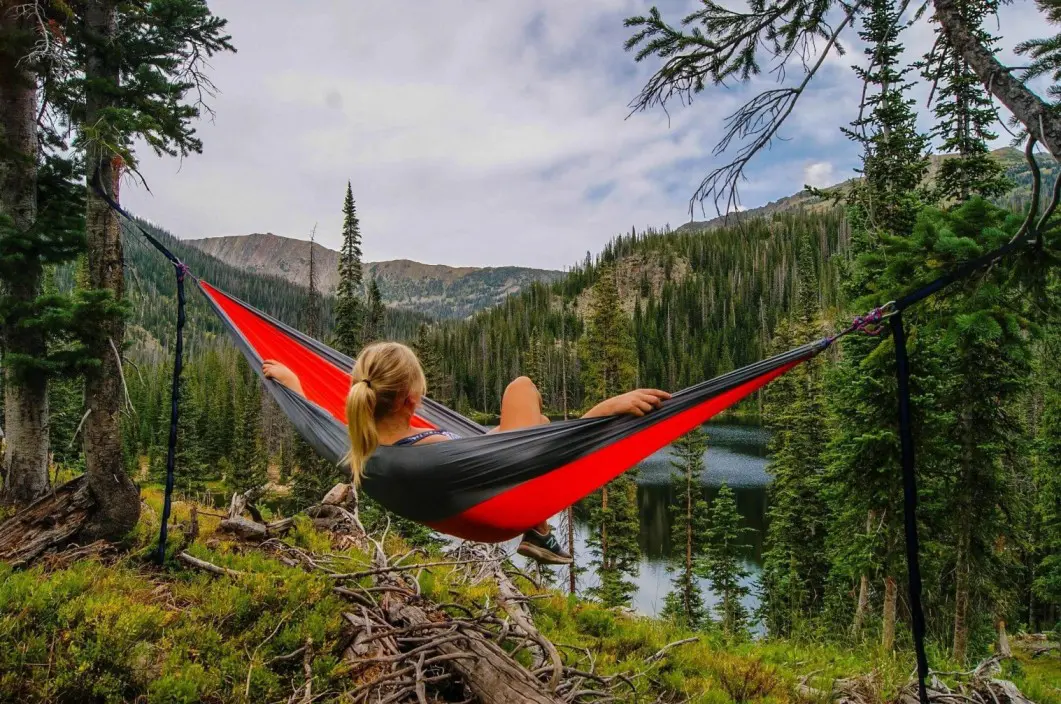 A young ethnic woman relaxes in quiet contemplation in a hammock suspended between two trees out in the forest. She is looking out over a mountain range.